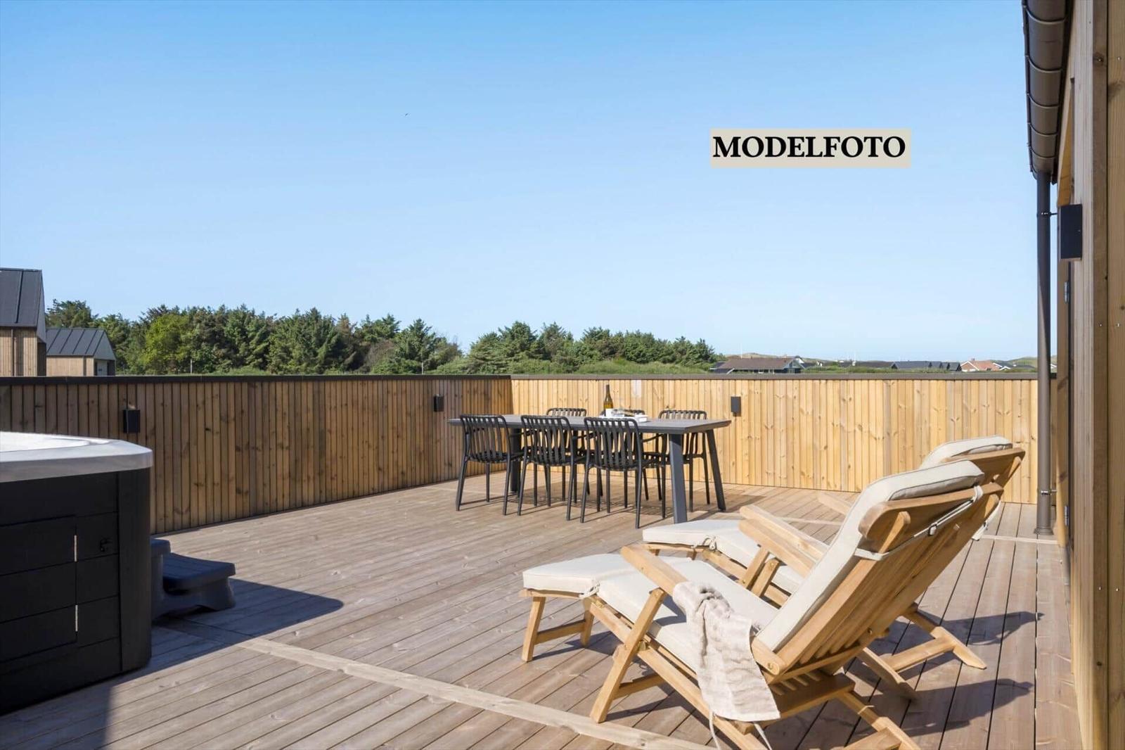 Terrasse mit Holzdielen, Liegestühlen, Esstisch und Whirlpool. Holzgeländer und Blick auf Bäume.