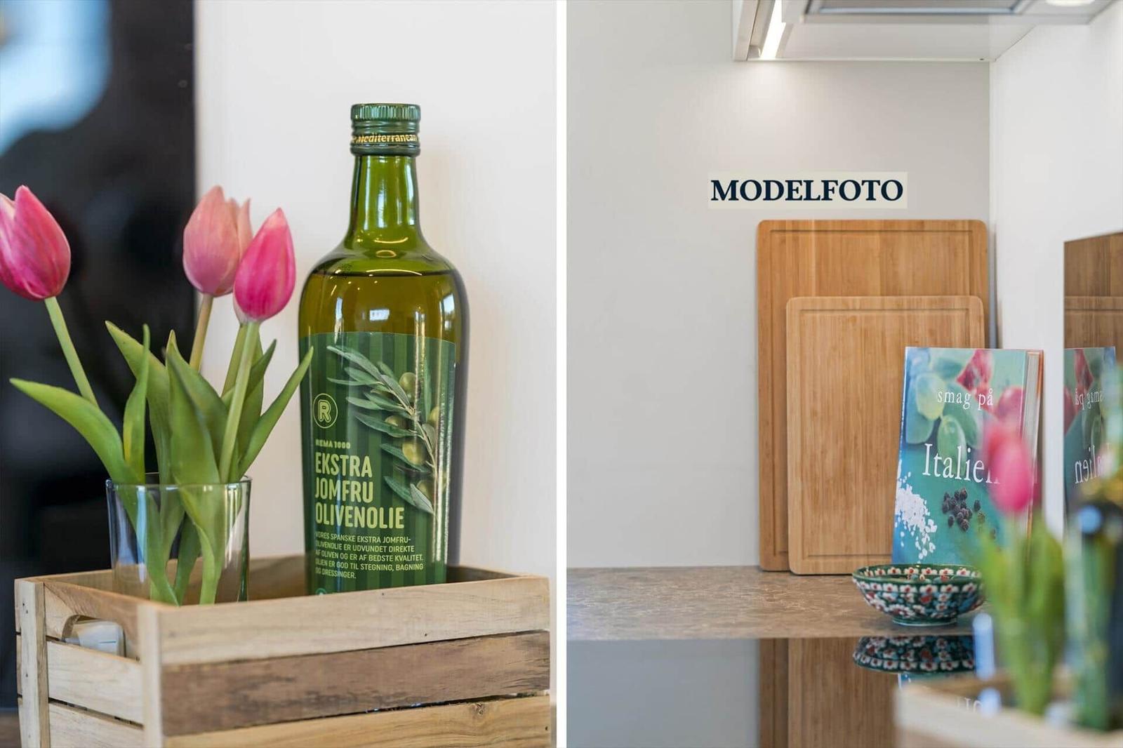 Küchenbereich mit Schneidebrettern, Kochbuch und Blumen. Flasche Olivenöl im Holzkasten.