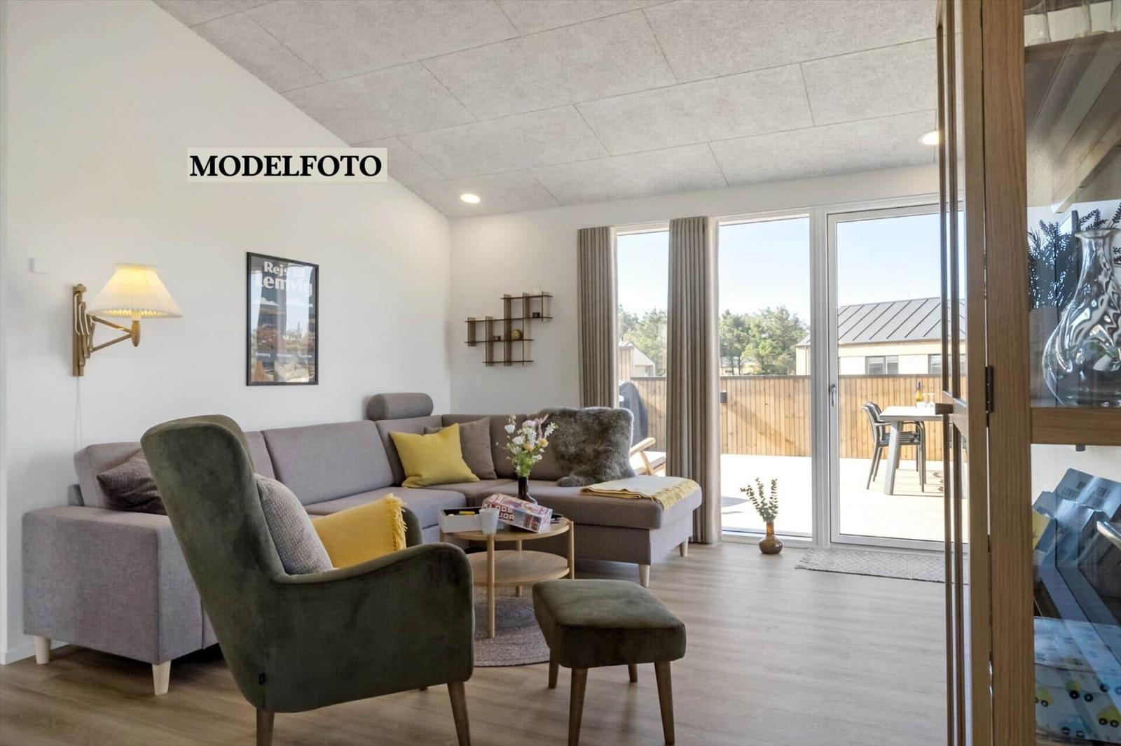 Wohnzimmer mit Sofa, Sessel und Terrasse. Durchgang zur Küche sichtbar.