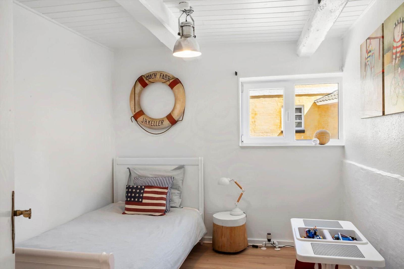 Ein Schlafzimmer mit weißer Wand, Bett, Fenster und Dekoration.