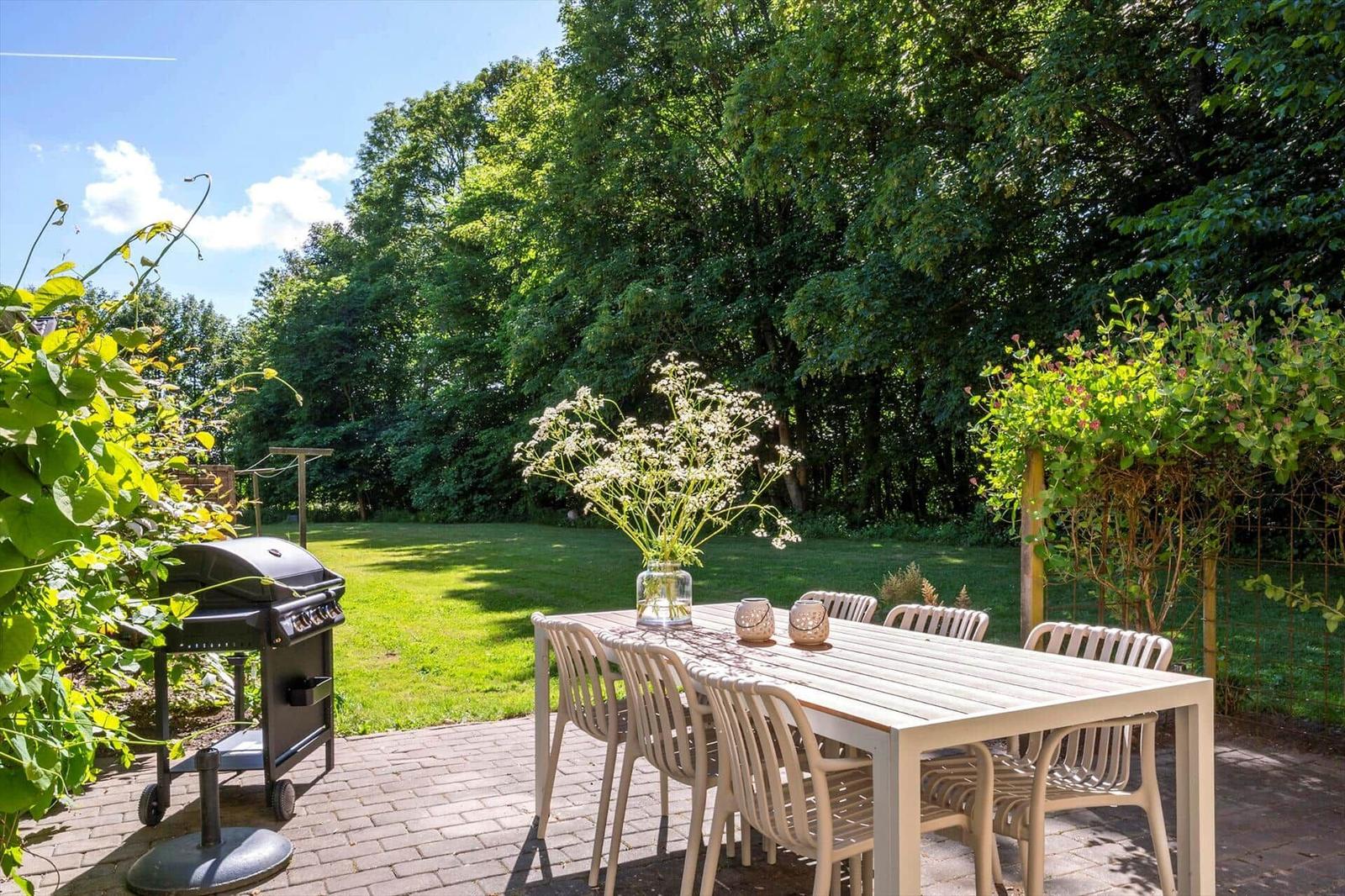 Terrasse mit Tisch, Stühlen, Grill und Blumenarrangement im Garten.