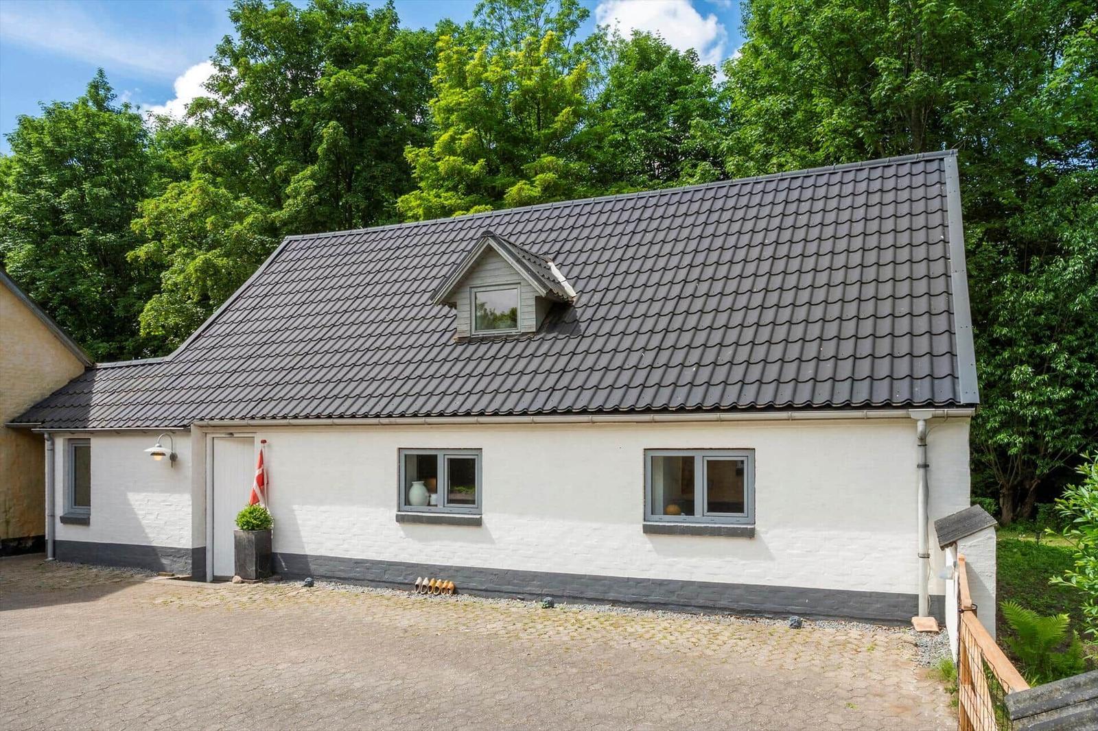 Ein weißes Haus mit grauem Dach und Fenstern, umgeben von Bäumen.