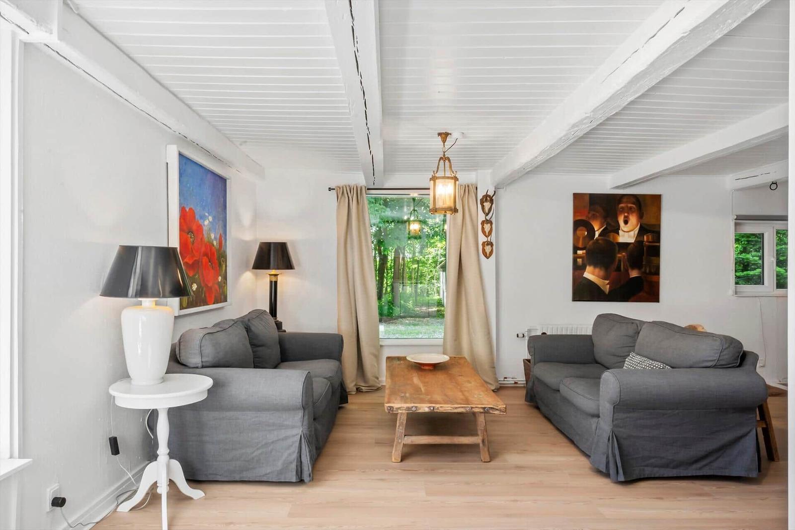 Wohnzimmer mit zwei grauen Sofas, Holztisch und Fenster zur grünen Umgebung.