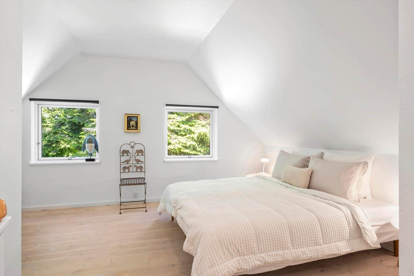 Schlafzimmer mit Dachschräge, zwei Fenstern und Bett mit Bettwäsche.