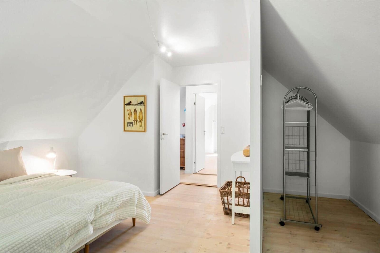 Schlafzimmer mit Dachschrägen, Bett, Kleiderständer und Tür zum Flur.