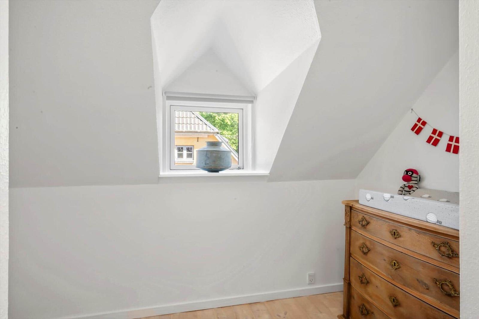Schlafzimmer mit Dachfenster, Holzschrank und dänischer Flaggenkette.