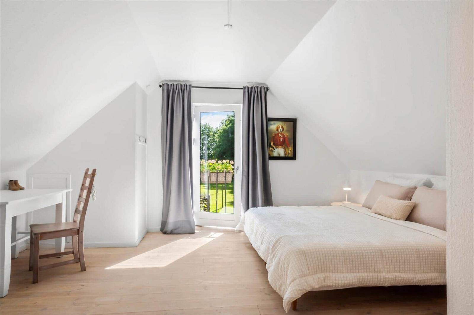 Schlafzimmer mit Dachschrägen, Bett, Schreibtisch und Tür zum Garten.