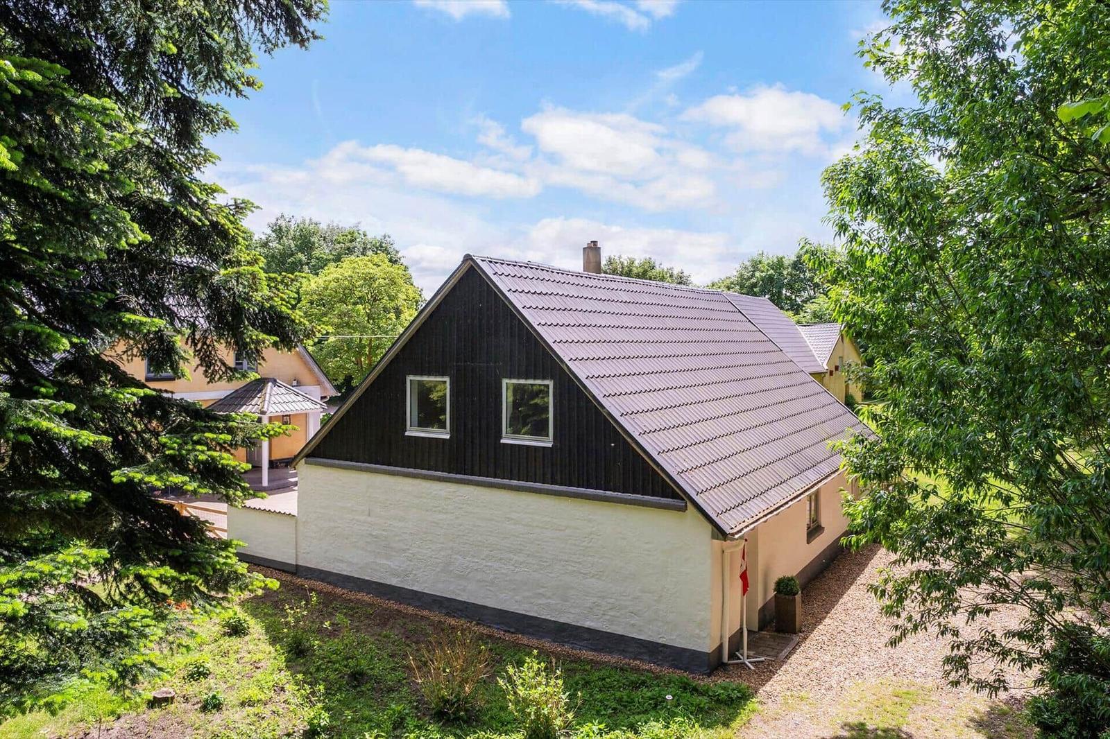Ein Haus mit dunklem Dach und hellen Wänden, umgeben von Bäumen und Grünflächen.