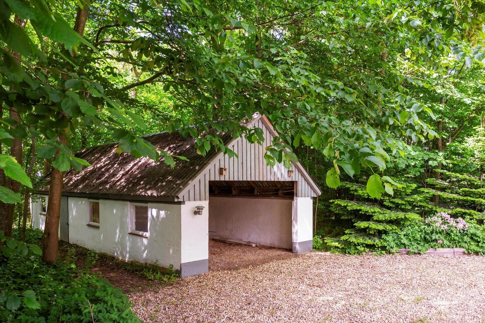 Ein kleines Haus mit Garage inmitten von Bäumen und Grünflächen.