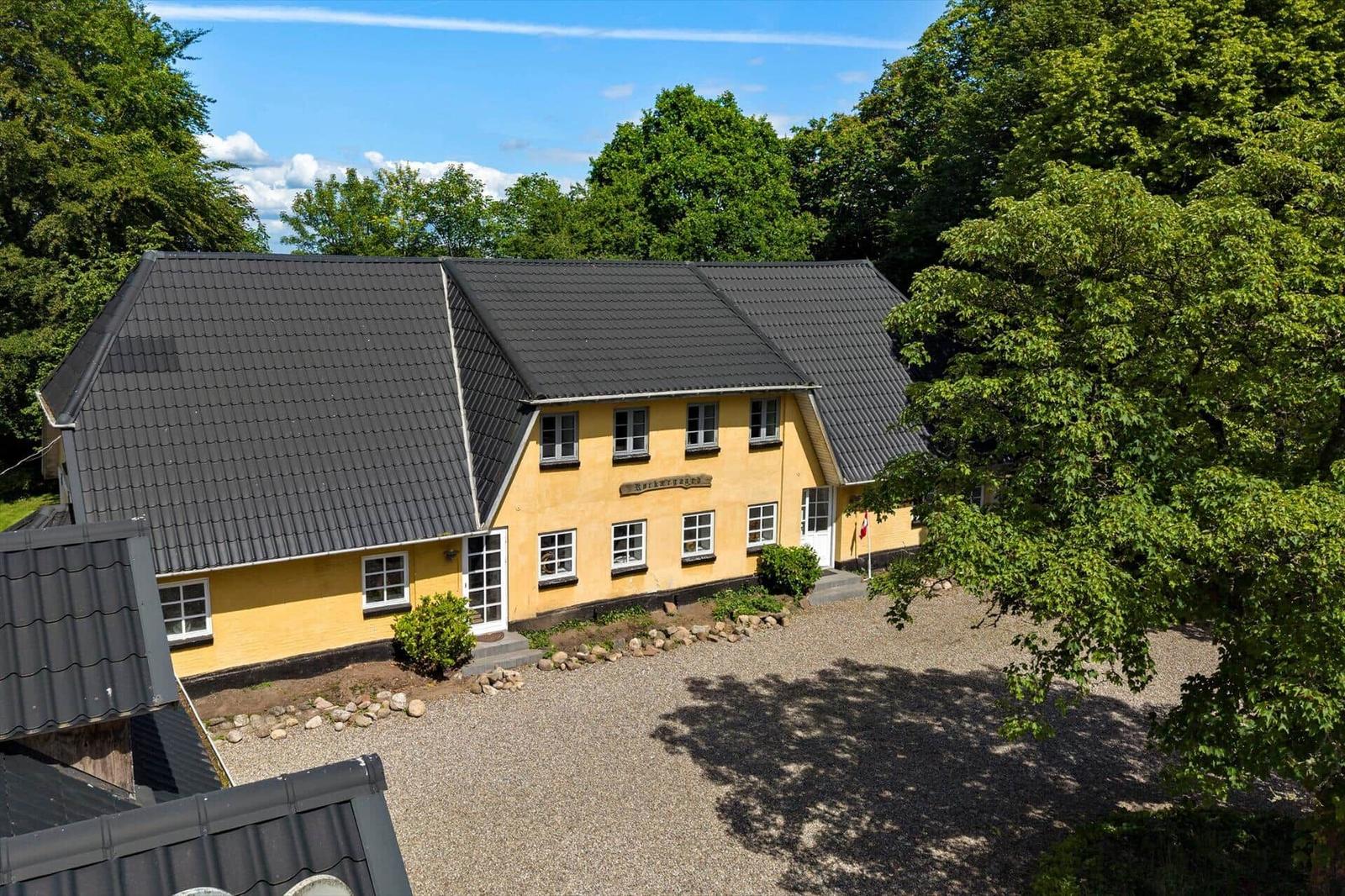 Ein gelbes Haus mit dunklem Dach und grüner Umgebung.