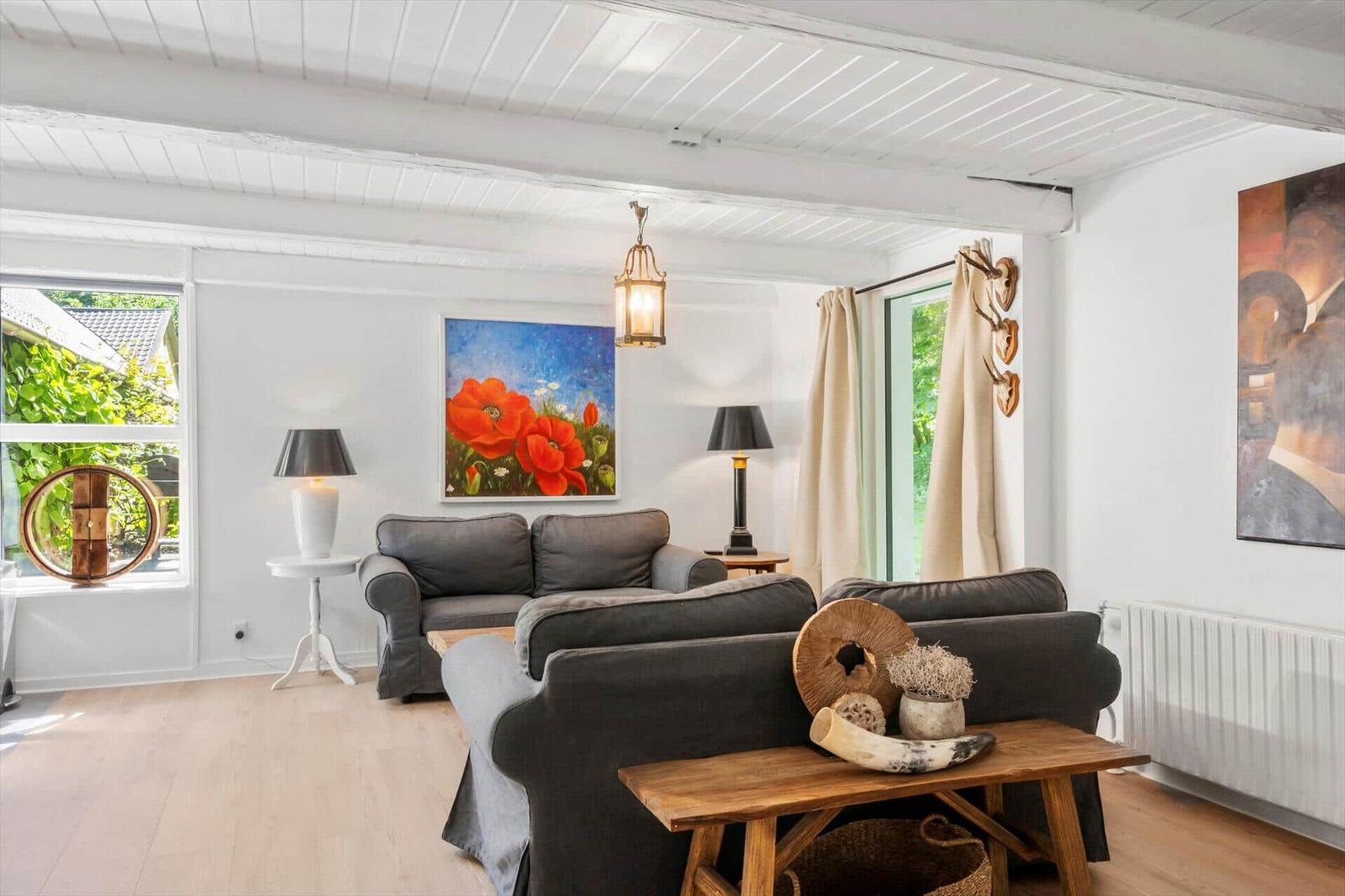 Wohnzimmer mit grauem Sofa, Holztisch und Gemälden an den Wänden.