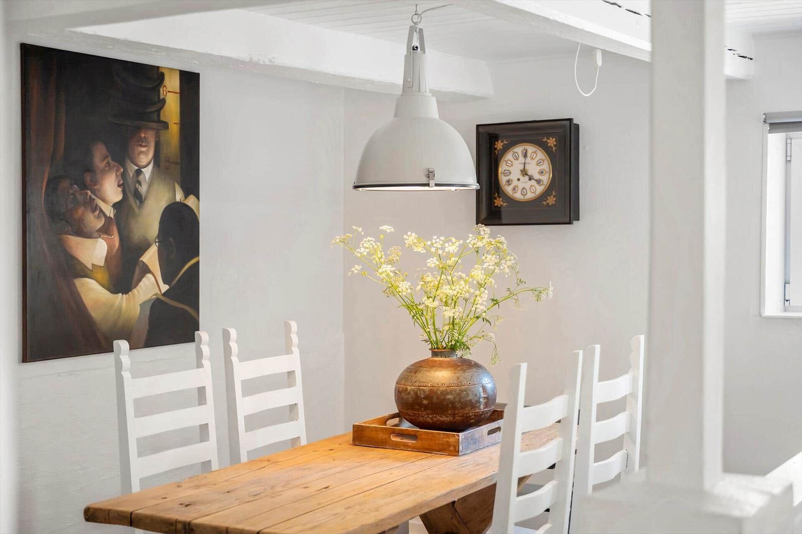 Esstisch mit weißen Stühlen, Blumen und Wanduhr unter einer Lampe.