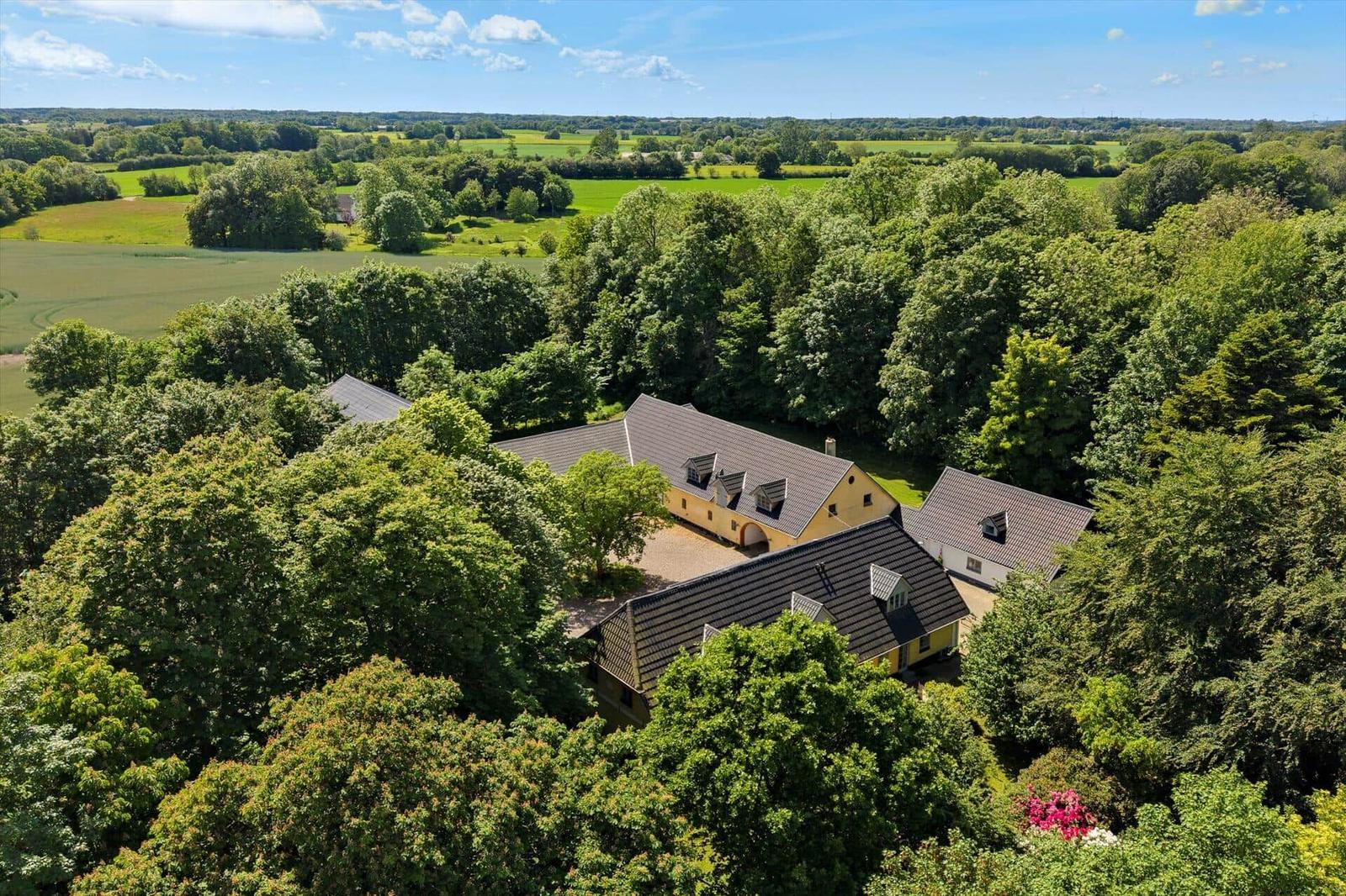 Haus mit Dachgauben und umliegenden Bäumen in ländlicher Umgebung.