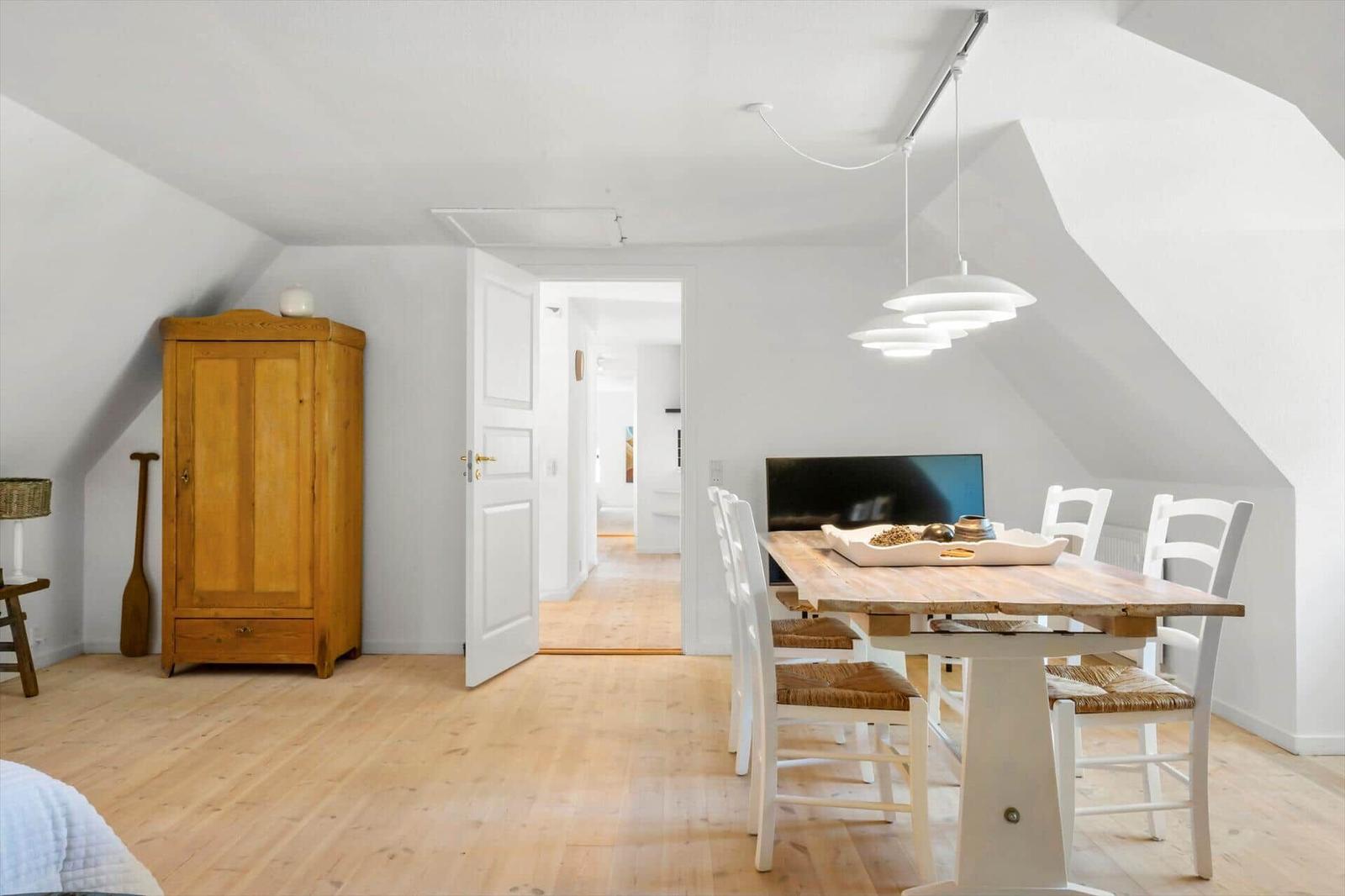 Essbereich mit Holztisch, weißen Stühlen und Schrank unter Dachschräge.