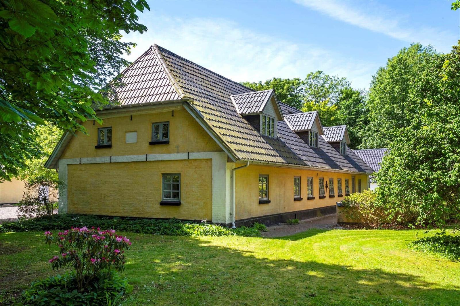 Ein gelbes Haus mit dunklem Dach und grüner Umgebung.