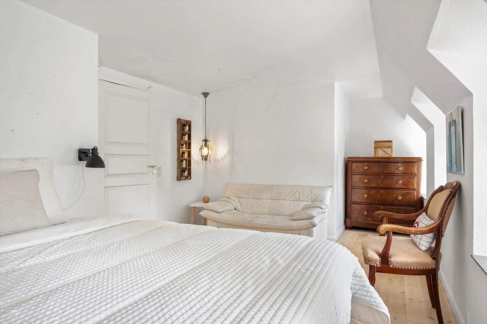 Schlafzimmer mit Bett, Sofa, Stuhl und Schrank unter Dachschräge.