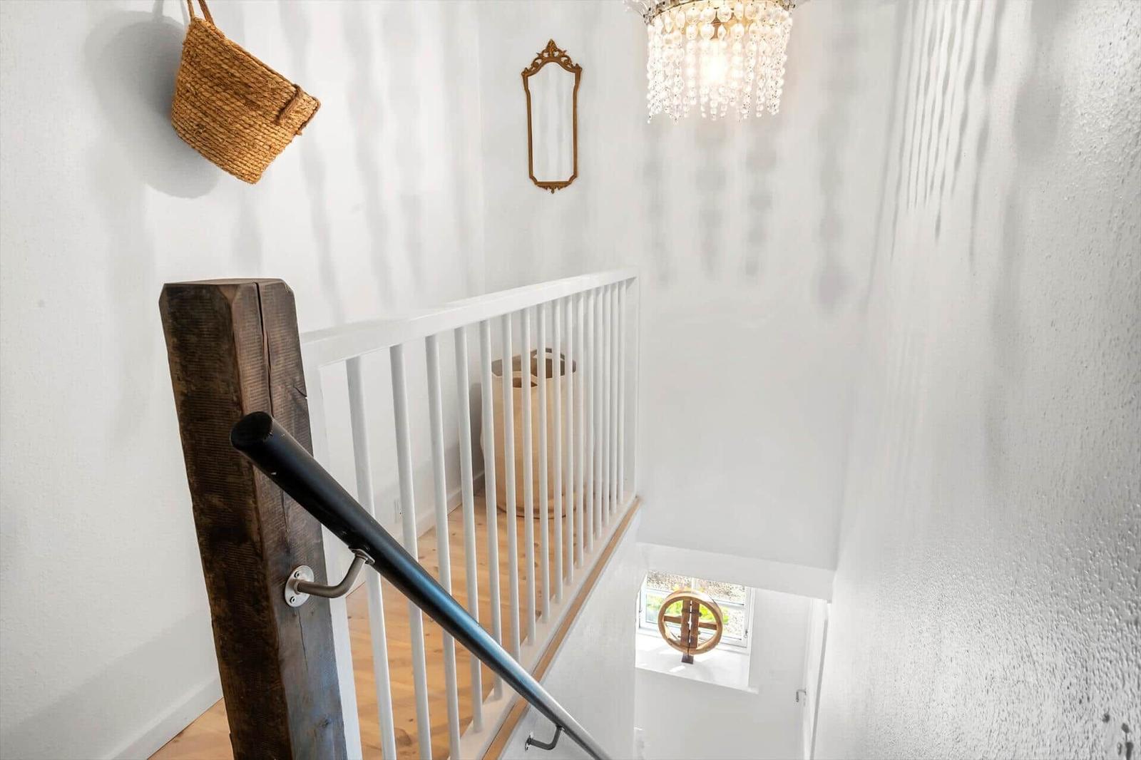 Helle Treppe mit weißer Balustrade und Holzgeländer. An der Wand hängt ein Korb und ein Spiegel.