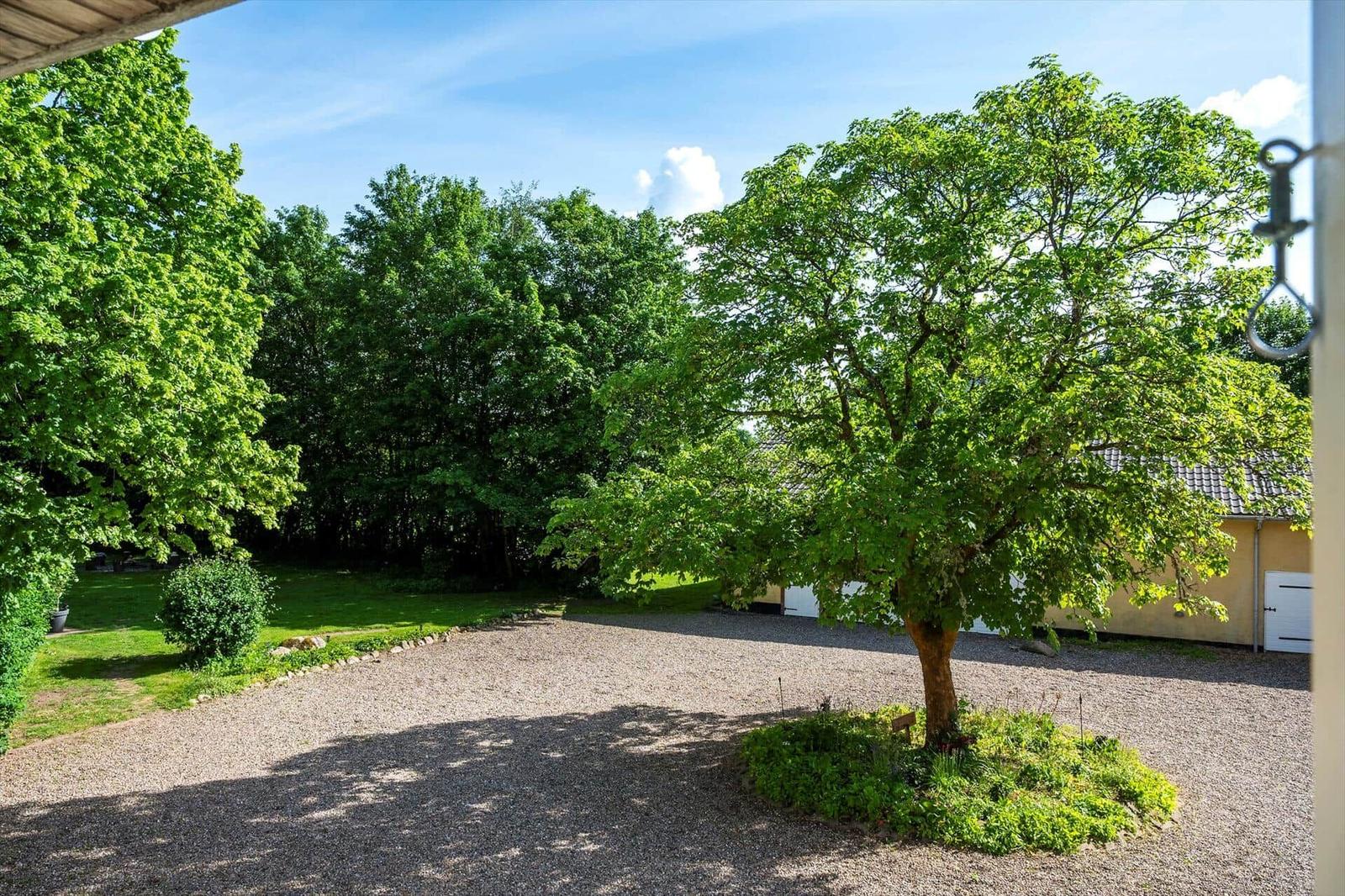 Garten mit Bäumen und Kiesfläche vor einem gelben Gebäude.