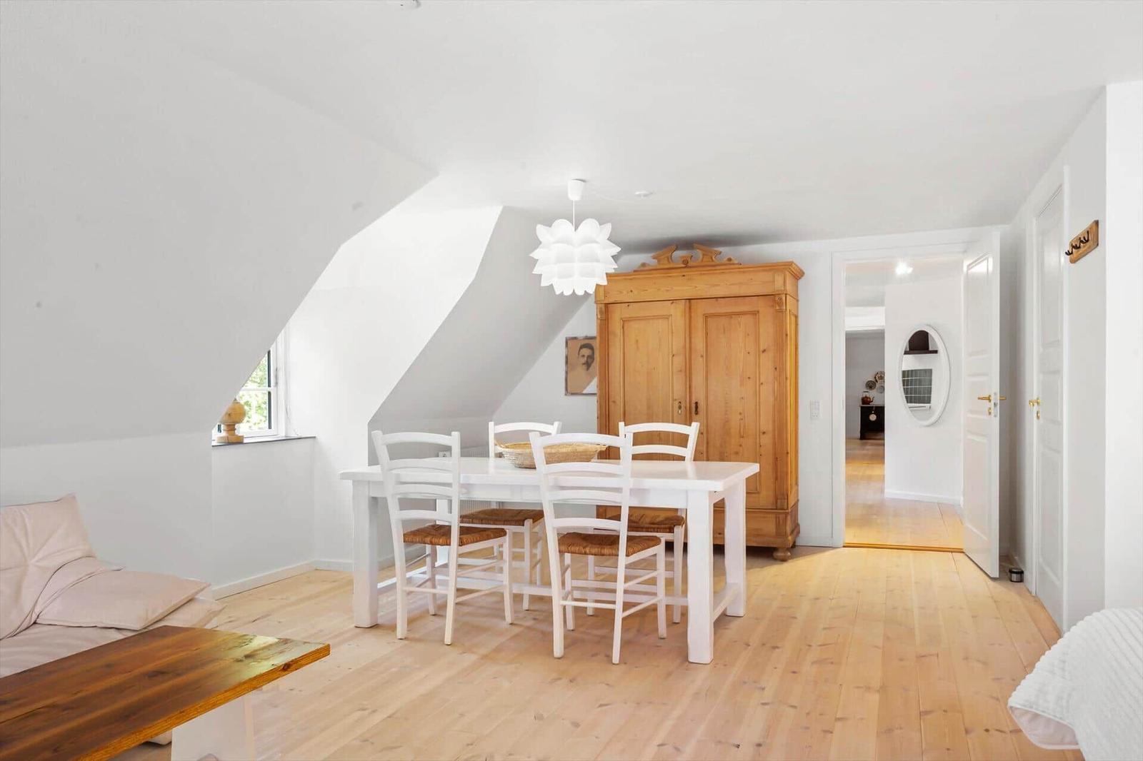 Wohn- und Essbereich mit Holzboden, weißem Tisch und Stühlen sowie einem Holzschrank.