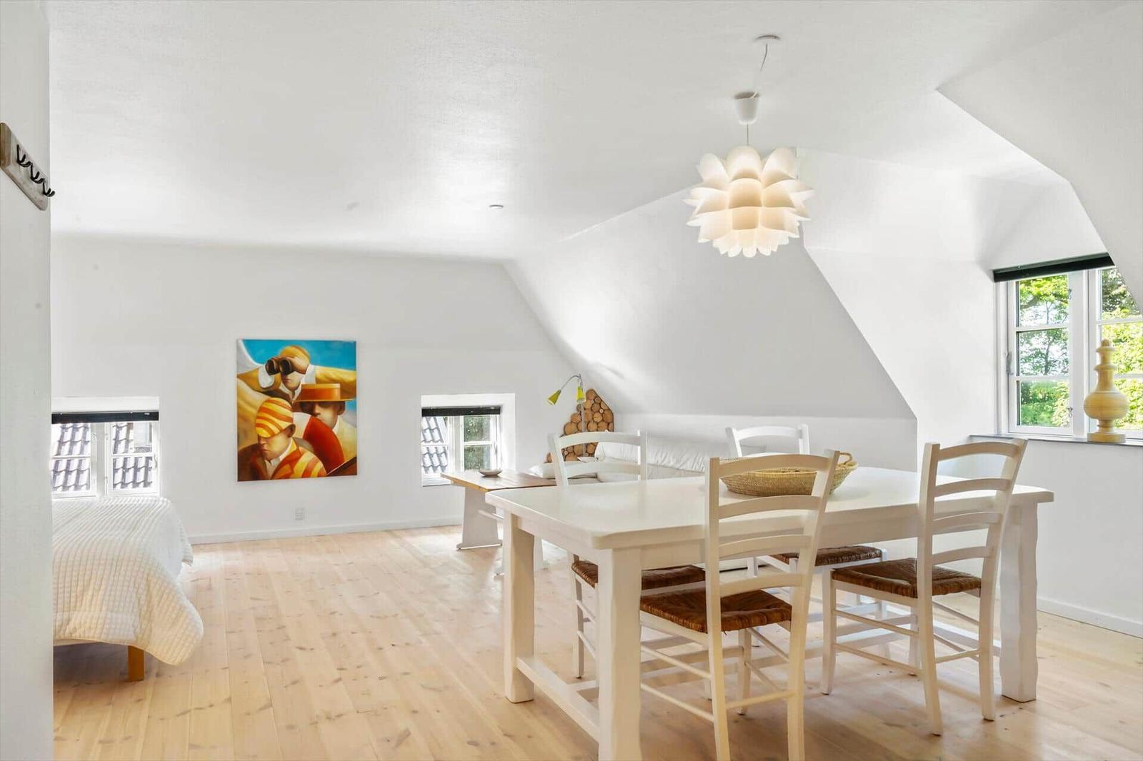 Wohnraum mit Esstisch, Bett und Wandbild unter schrägen Dachdecken.