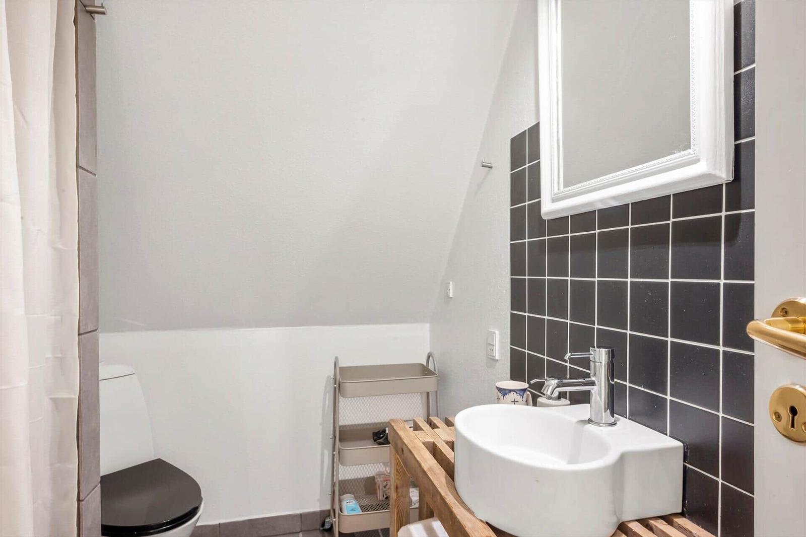 Badezimmer mit Waschbecken, Spiegel und Toilette. Wand mit dunklen Fliesen.