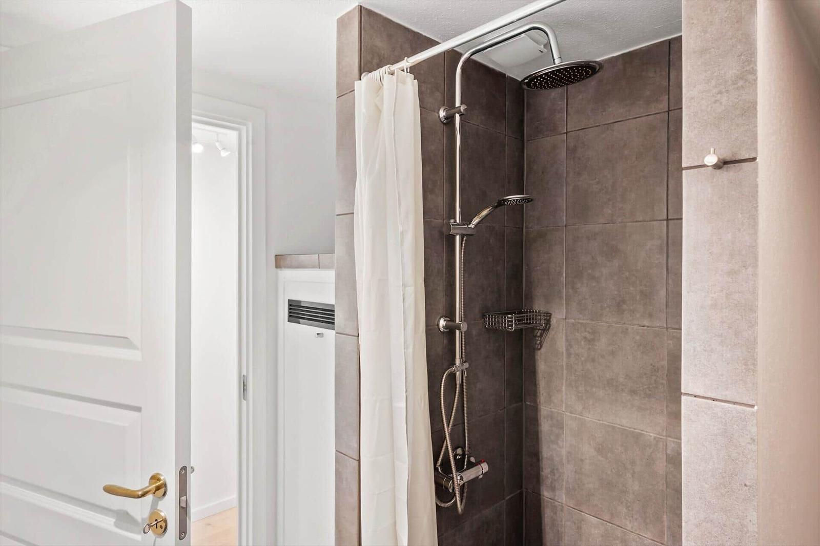 Dusche mit Duschbrause und Vorhang in moderner Badezimmerausstattung.