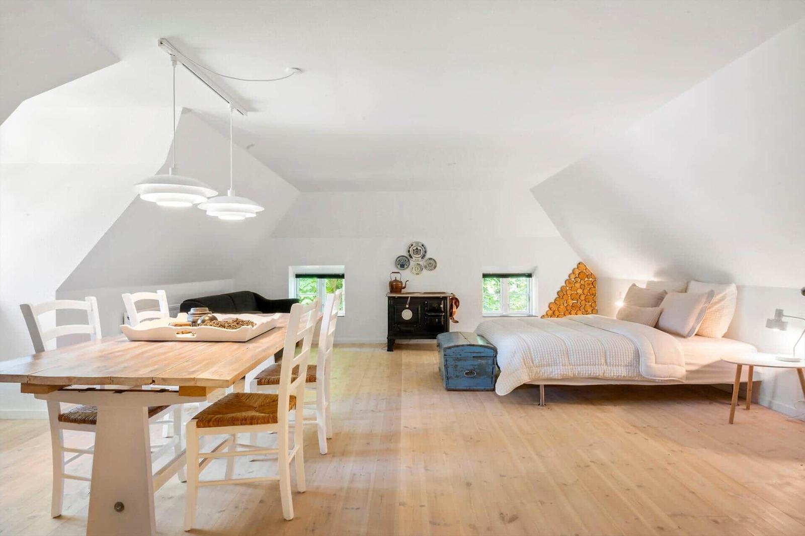 Ein Raum mit Bett, Esstisch und Holzfußboden unter schrägen Wänden.