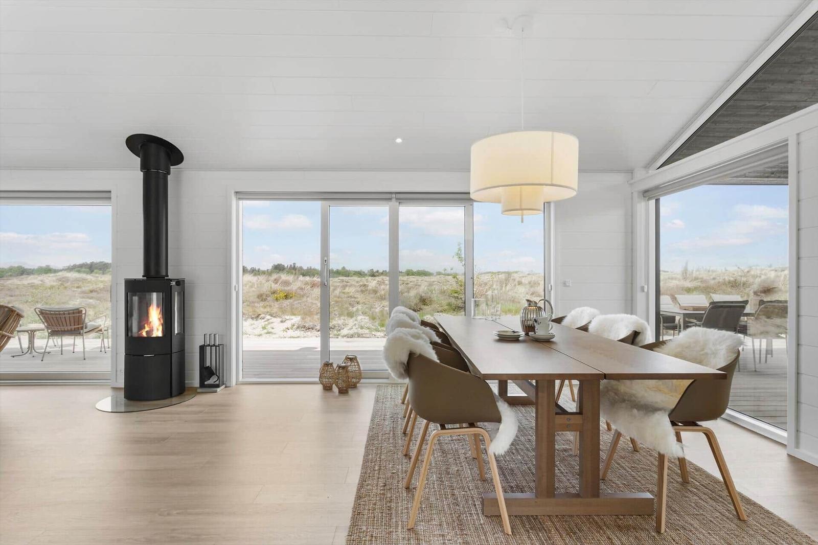 Essbereich mit Tisch, Stühlen und Kamin. Große Fenster zeigen Landschaft.