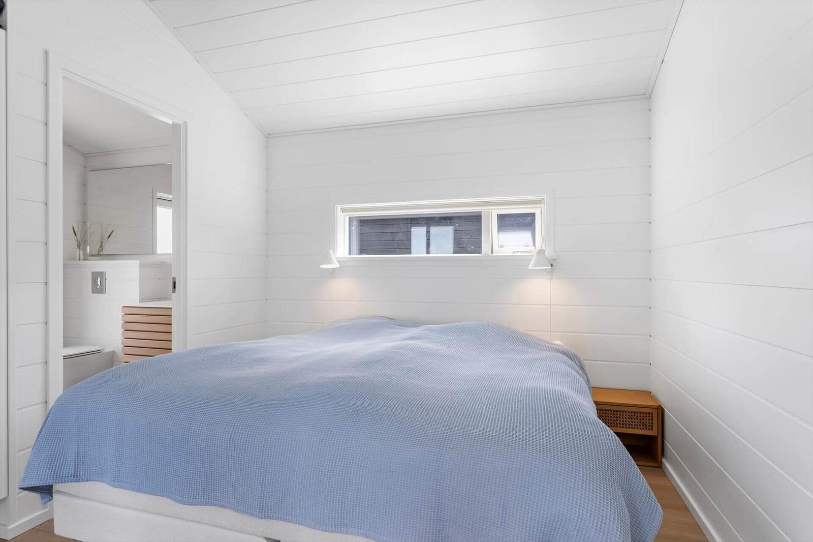 Schlafzimmer mit Bett, Fenster und Nachttisch. Badezimmer im Anschluss.