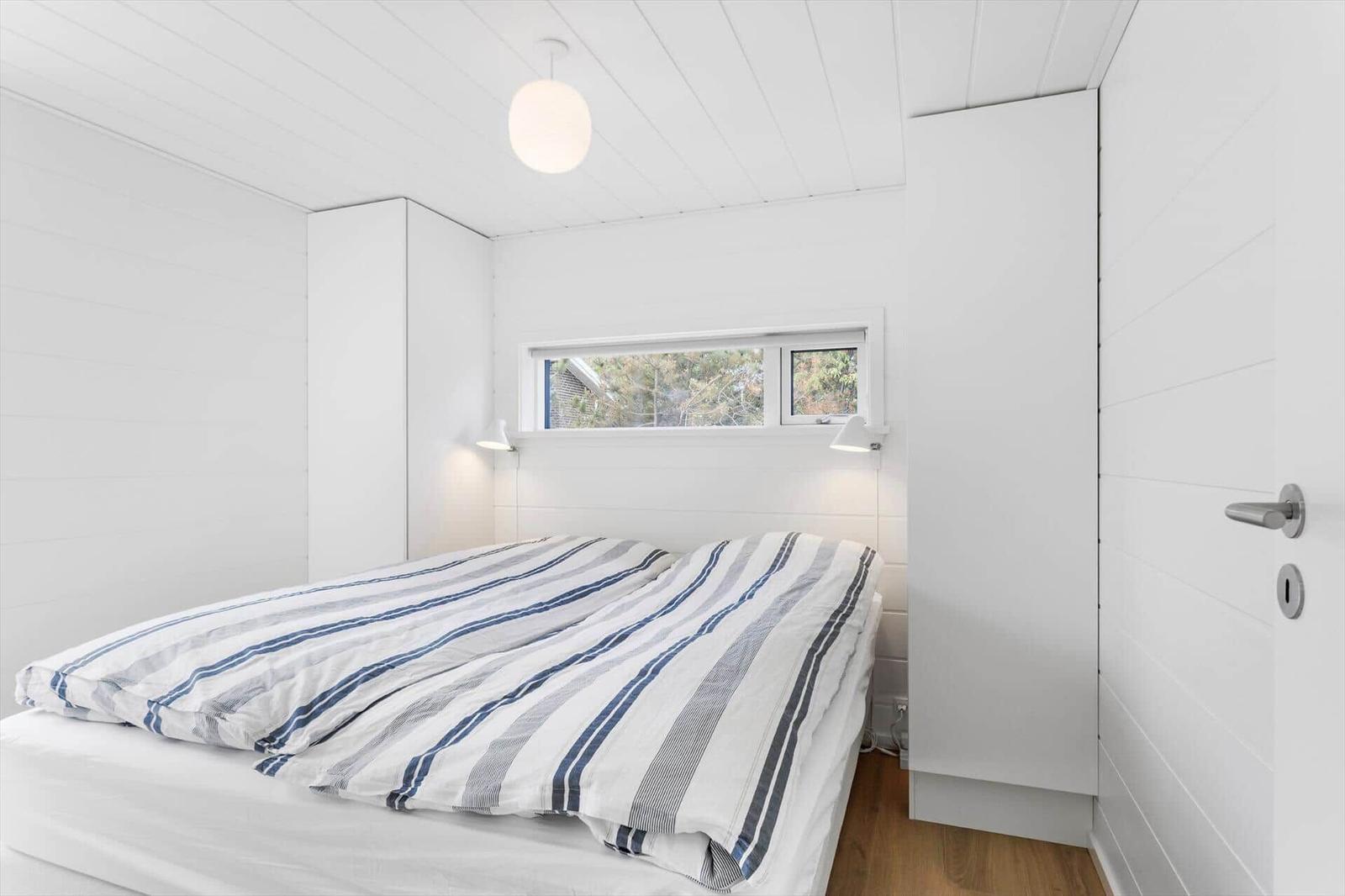 Schlafzimmer mit Bett, Fenster und weißen Wänden.