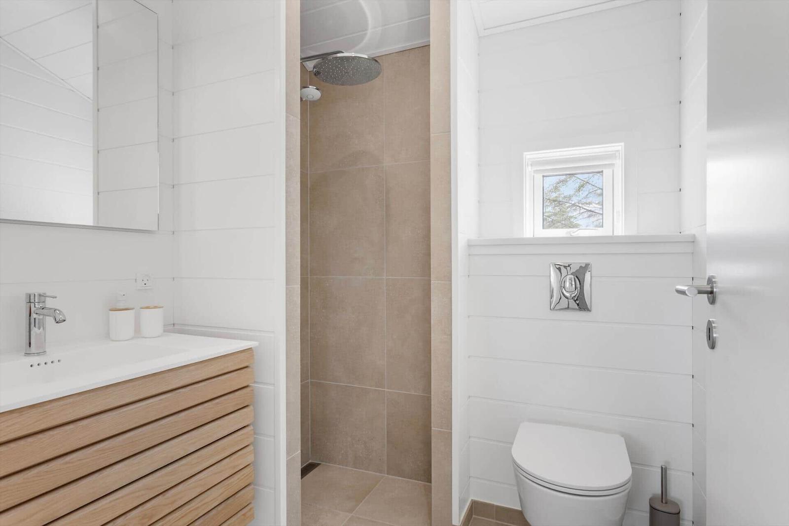 Badezimmer mit Dusche, Waschbecken und Toilette. Weiße Wände und Holzunterschrank.