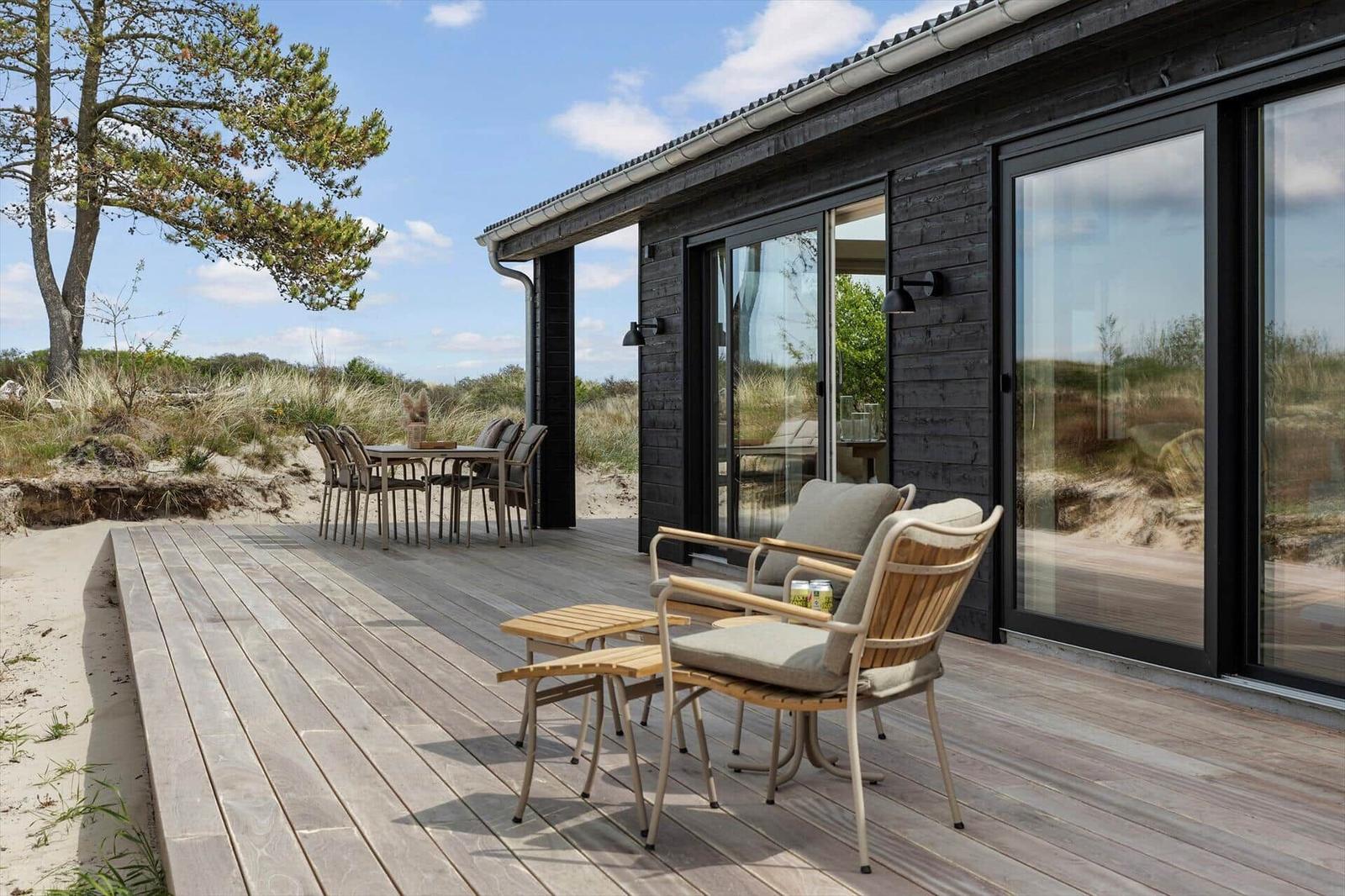 Terrasse mit Sitzgruppe und Esstisch. Holzdecke, Schiebetüren und Blick auf Dünen.
