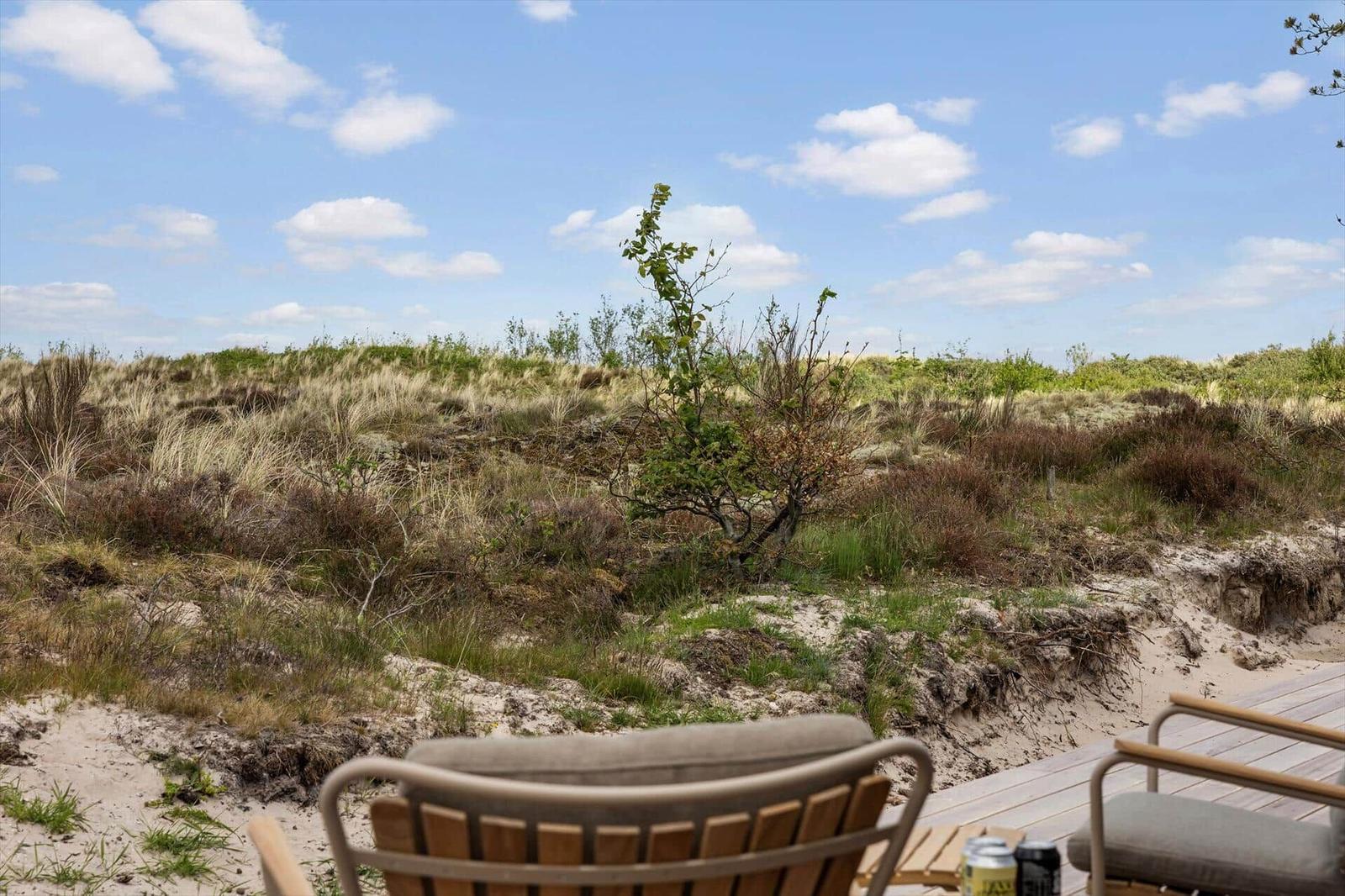Terrasse mit Stühlen und Blick auf Dünenlandschaft unter blauem Himmel.