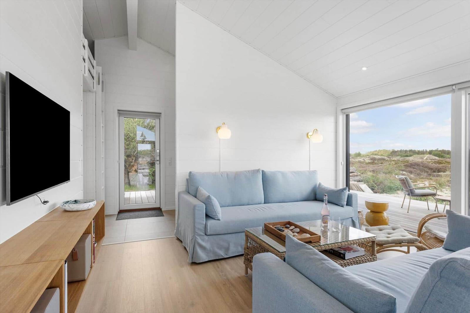 Wohnzimmer mit Sofa, Fernseher und Blick auf die Landschaft.