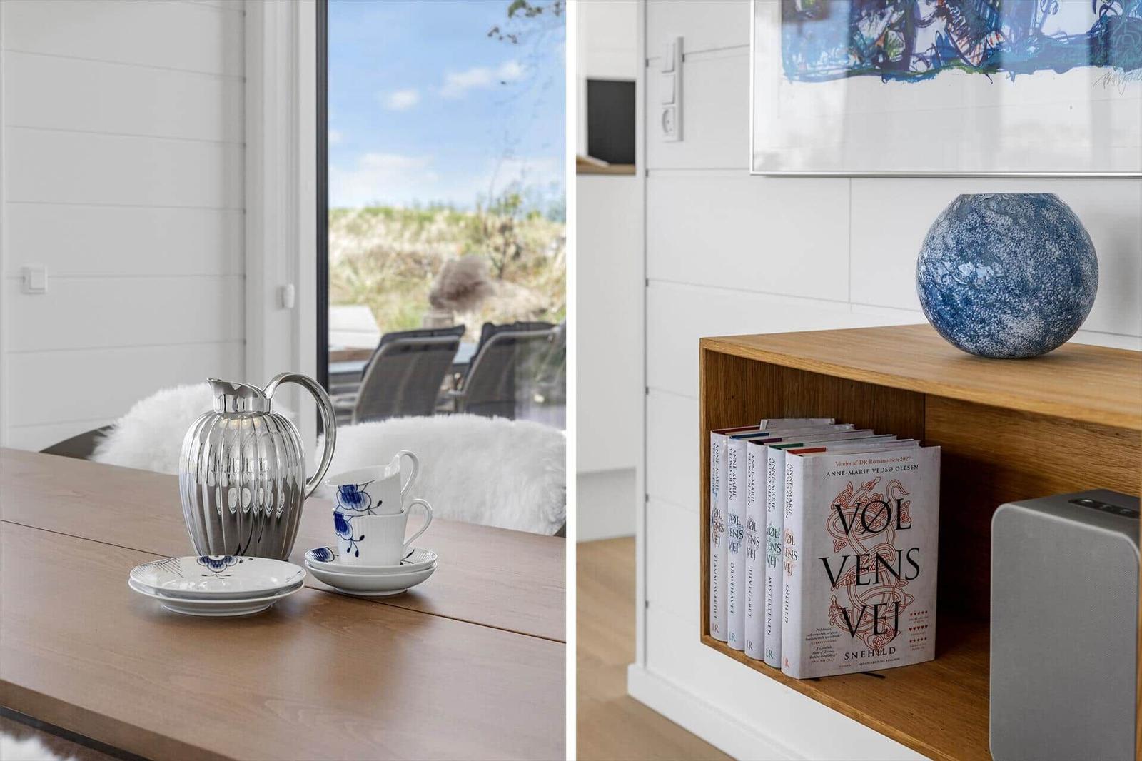 Esstisch mit Porzellan und Blick auf Terrasse. Holzregal mit Büchern und blauem Vasen.