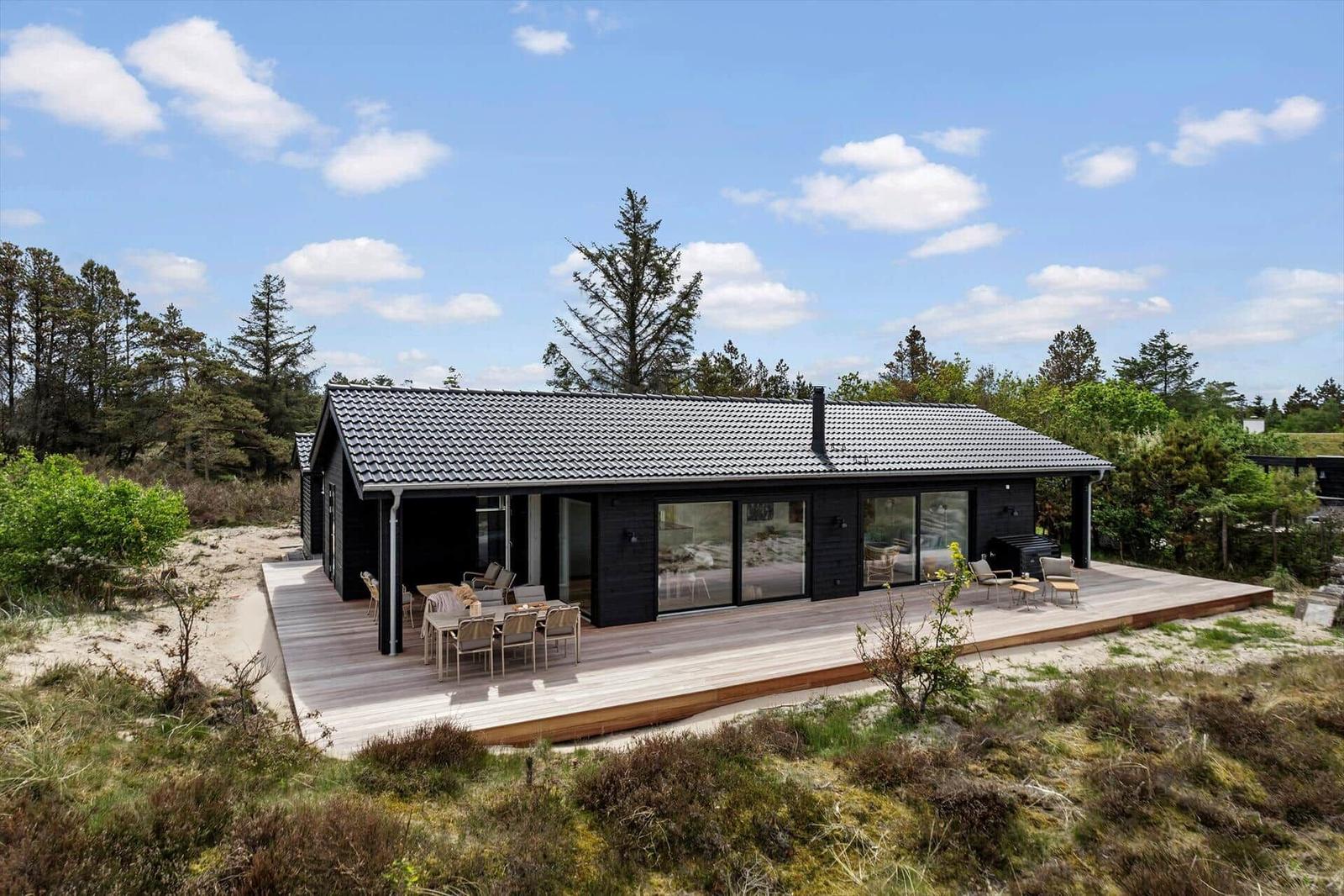 Moderne Villa mit großem Holzterrasse, Gartentisch und -stühlen. Umgeben von Bäumen und Gras.