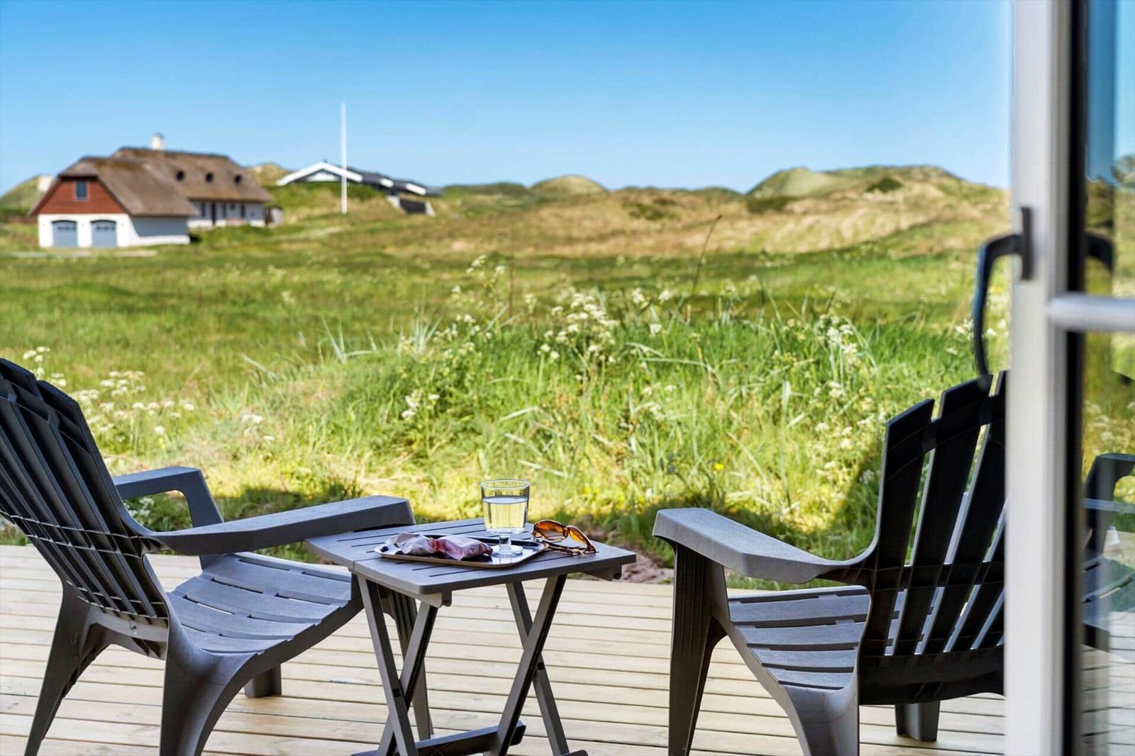 Terrasse mit zwei Stühlen und Tisch. Blick auf grüne Wiesen und Häuser im Hintergrund.