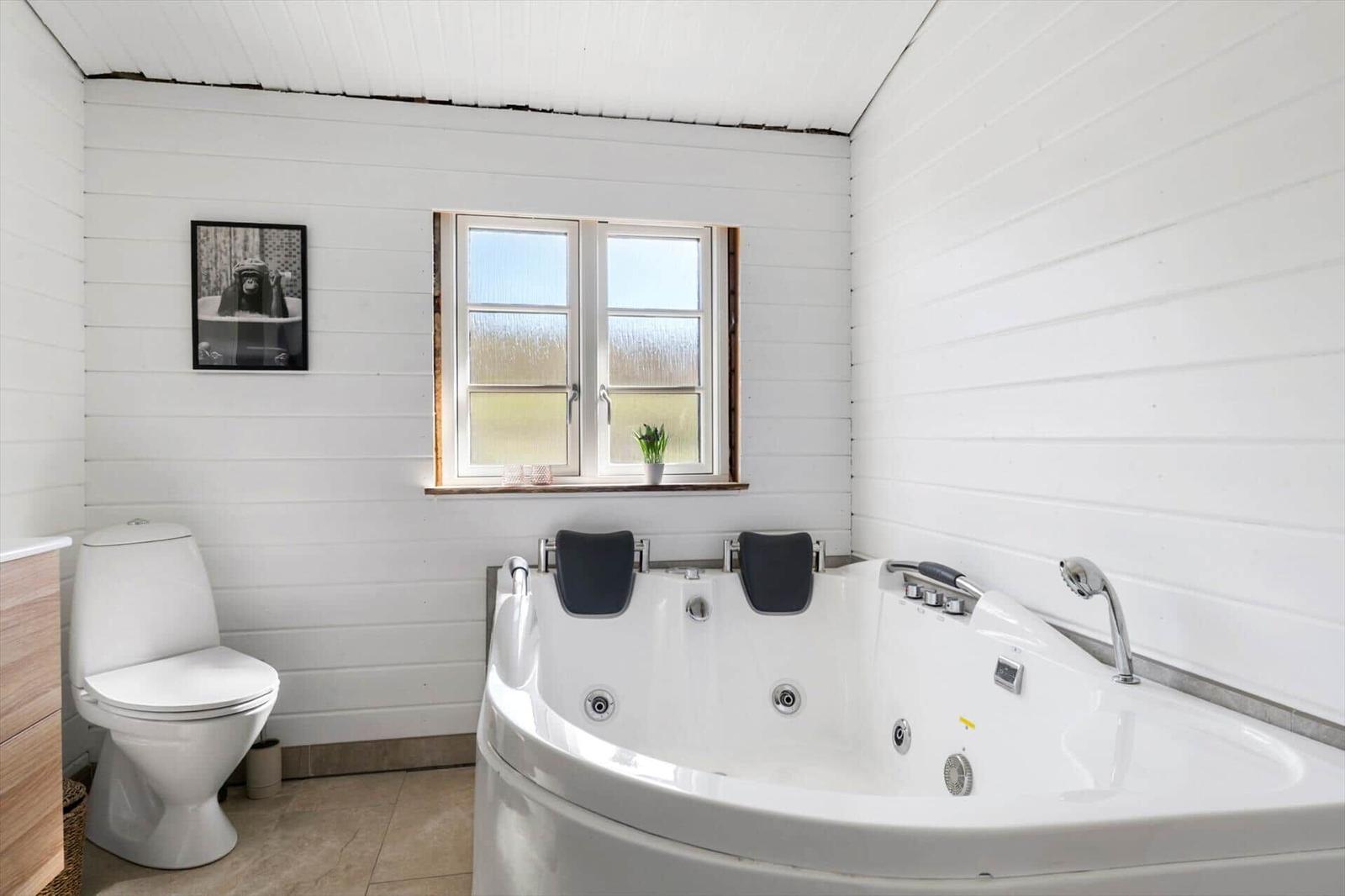 Badezimmer mit Whirlpool, Toilette und Fenster mit Pflanze.