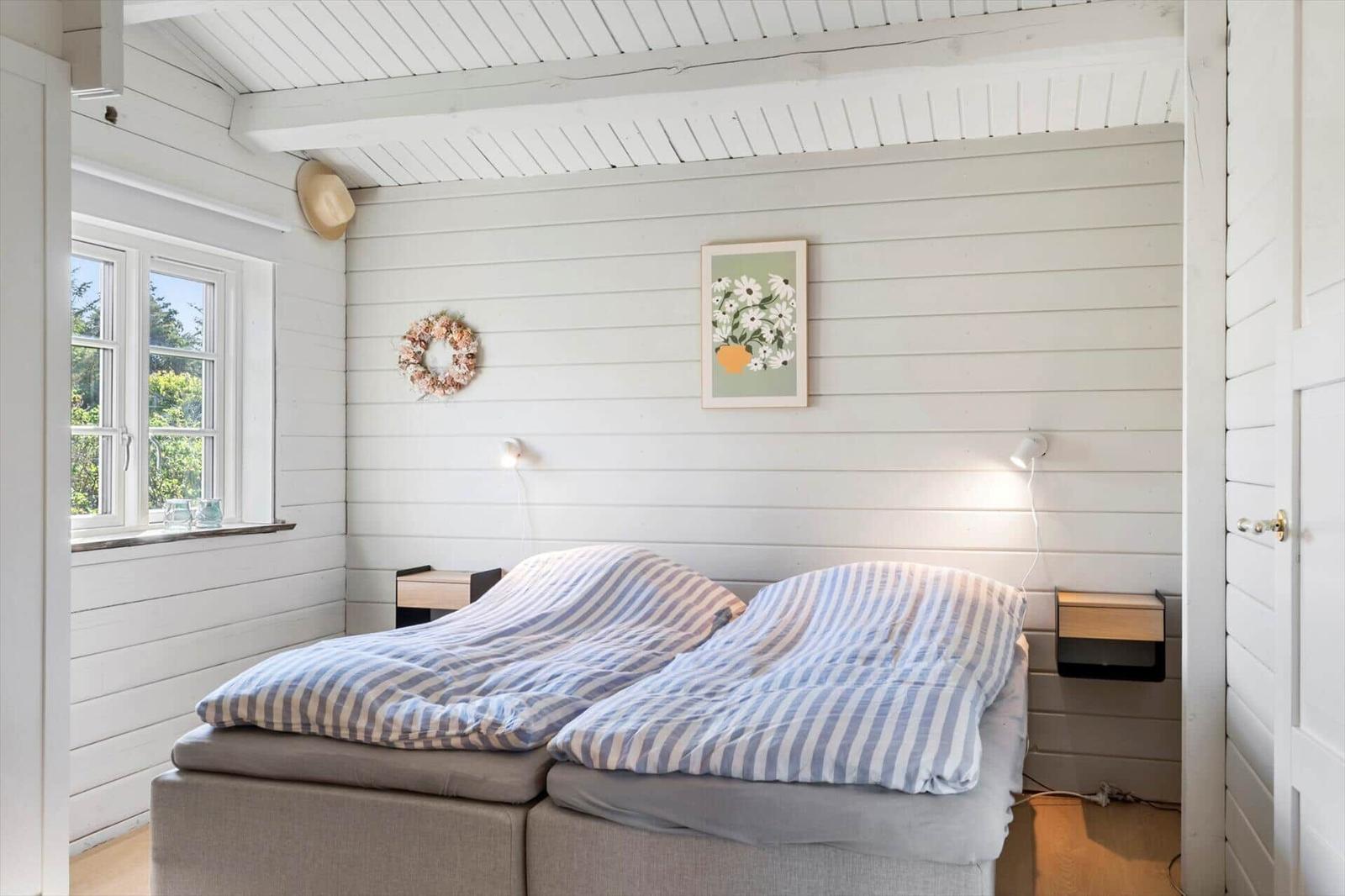 Schlafzimmer mit Doppelbett, weißen Wänden und Fenster mit Blick auf Grün.