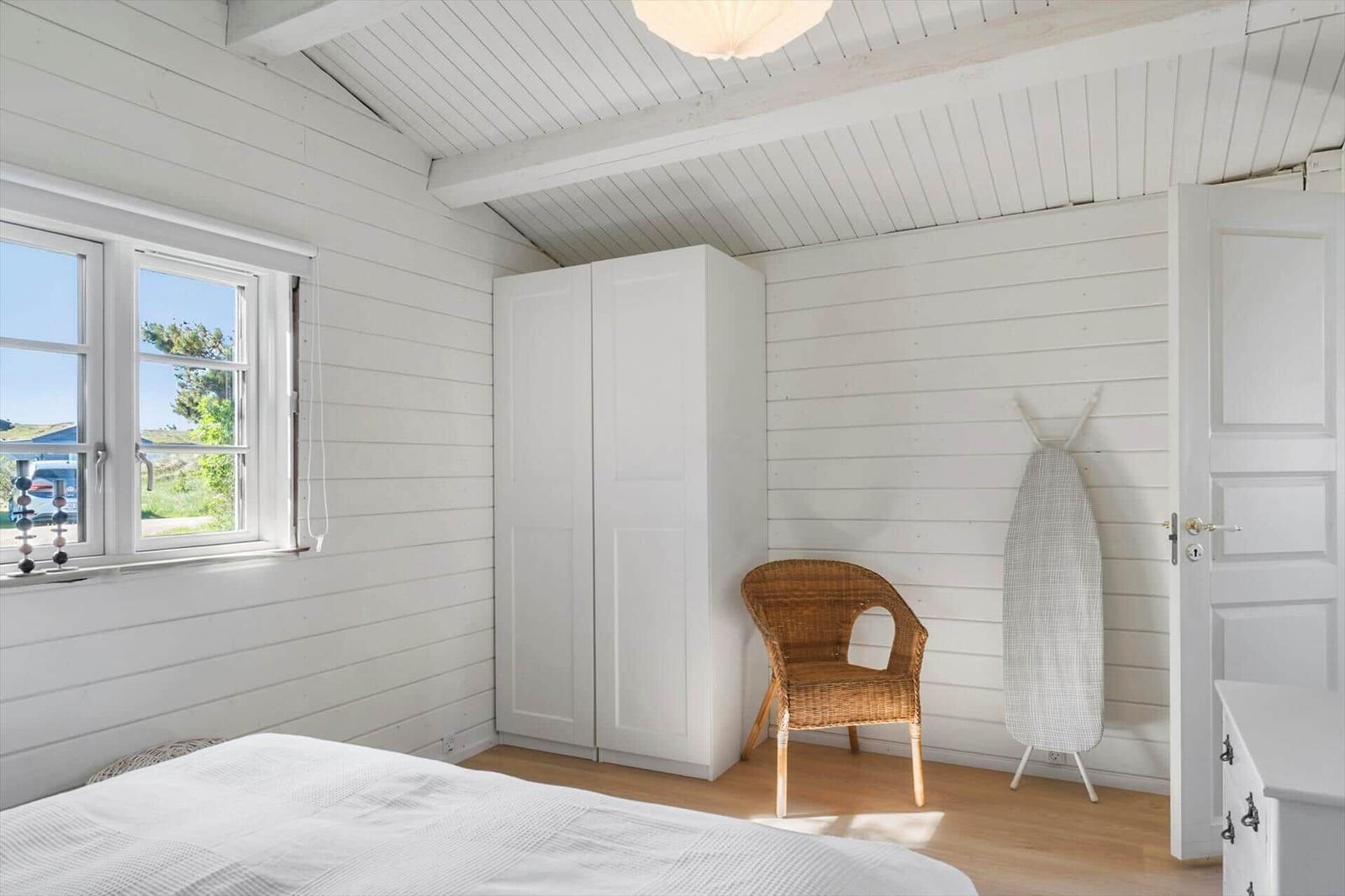 Schlafzimmer mit weißem Schrank, Wickerstuhl und Blick auf die Außenseite.