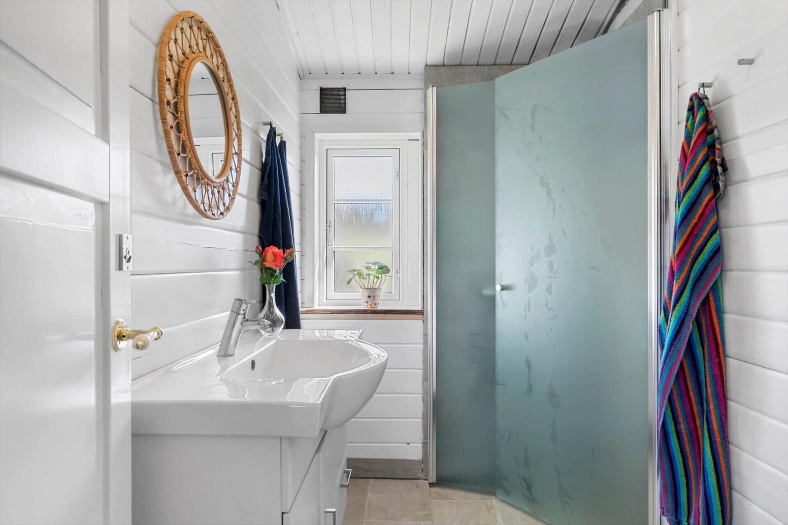Badezimmer mit Dusche, Waschbecken und Fenster. Wände sind weiß verputzt.
