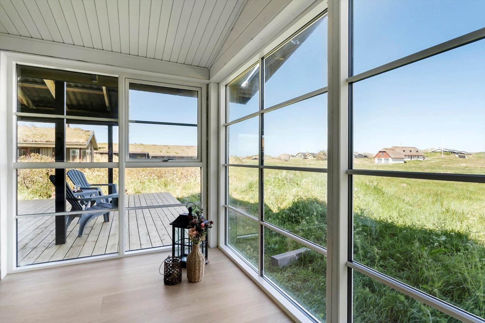 Große Fensterfront mit Blick auf grünes Feld und Terrasse mit Stühlen.
