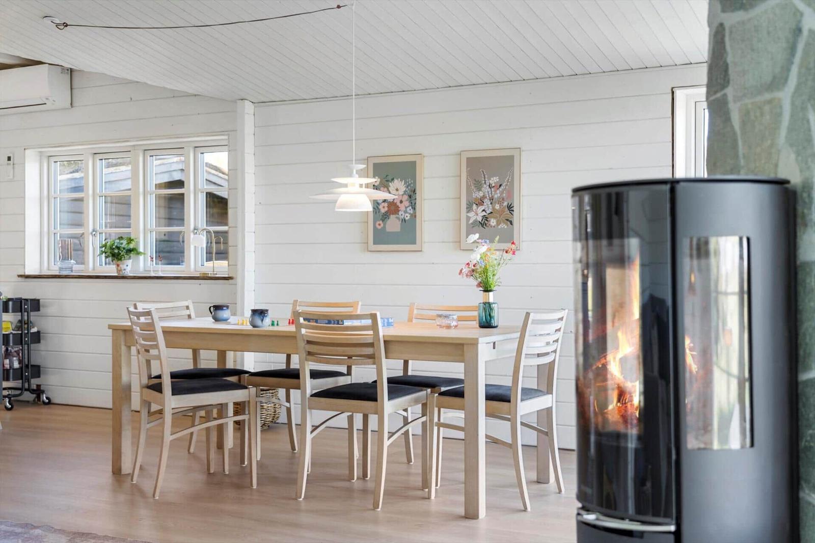Esszimmer mit Holztisch, Stühlen und Kaminofen. An der Wand hängen zwei Bilder.