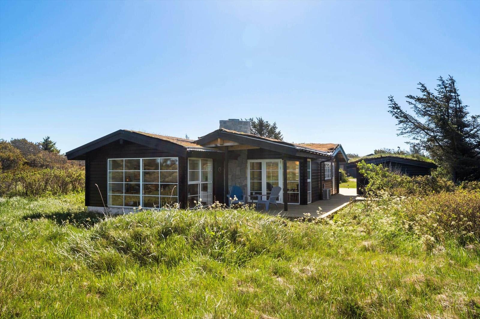 Moderne Holzhütte mit Terrasse und großen Fenstern in grüner Umgebung.