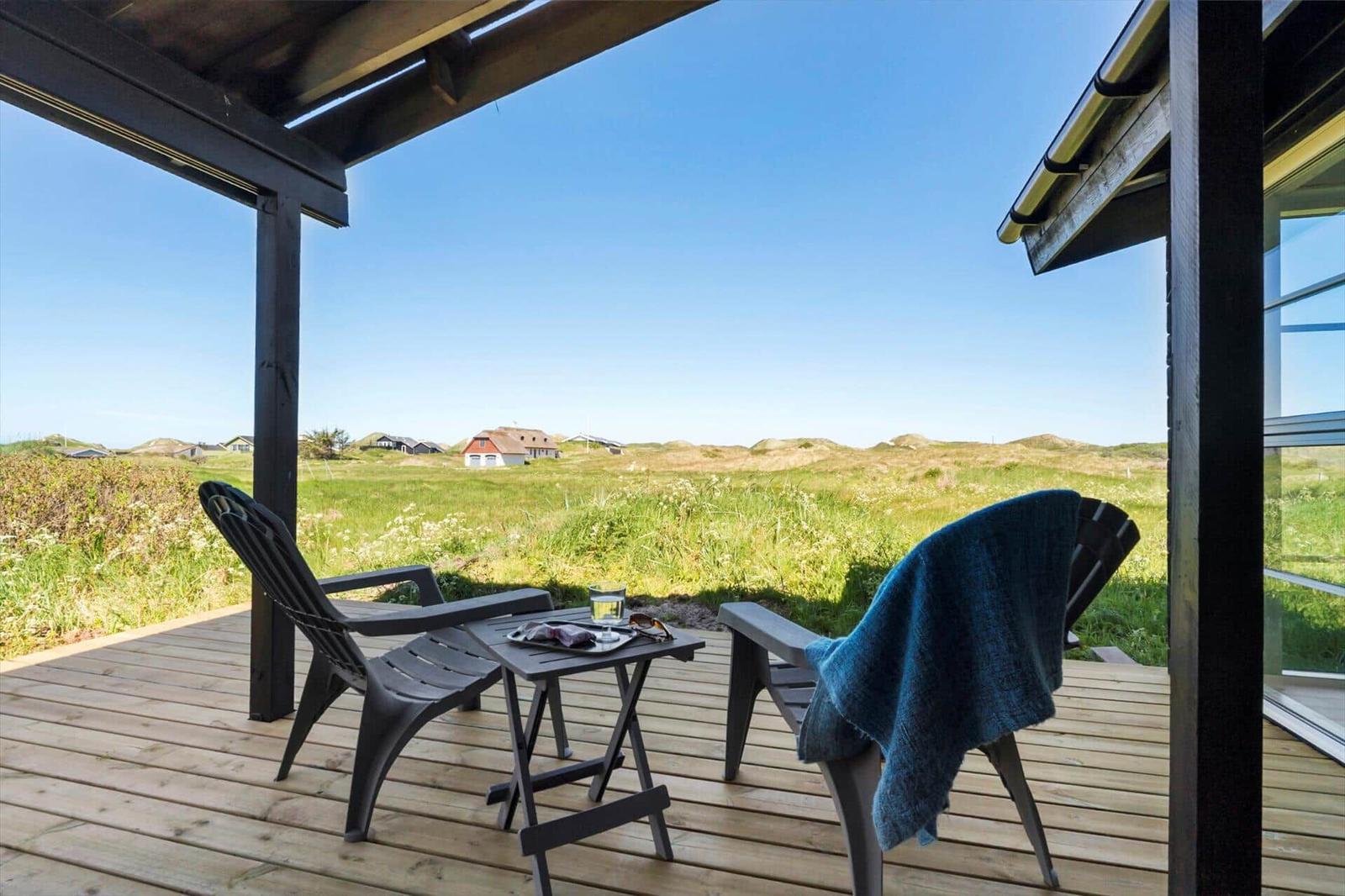 Terrasse mit zwei Stühlen und Tisch, Blick auf grüne Wiesen und Häuser.