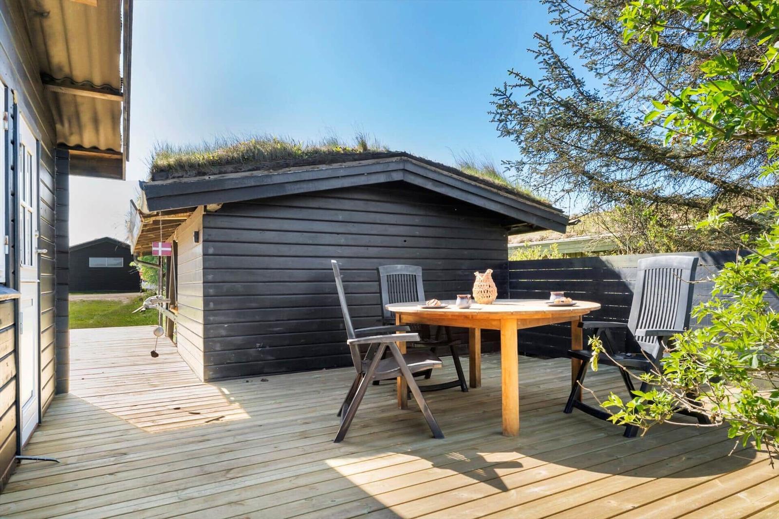 Holzterrasse mit Tisch und Stühlen vor einem Haus mit Grasdach.