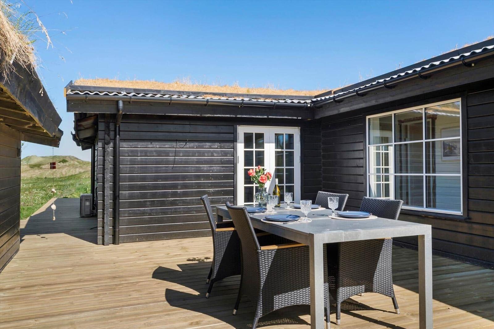 Terrasse mit Esstisch und Stühlen vor einem Haus mit Grasdach und Holzwand.