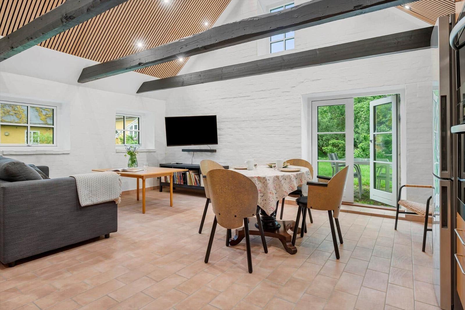 Living and dining area with beams, TV, and terrace door.