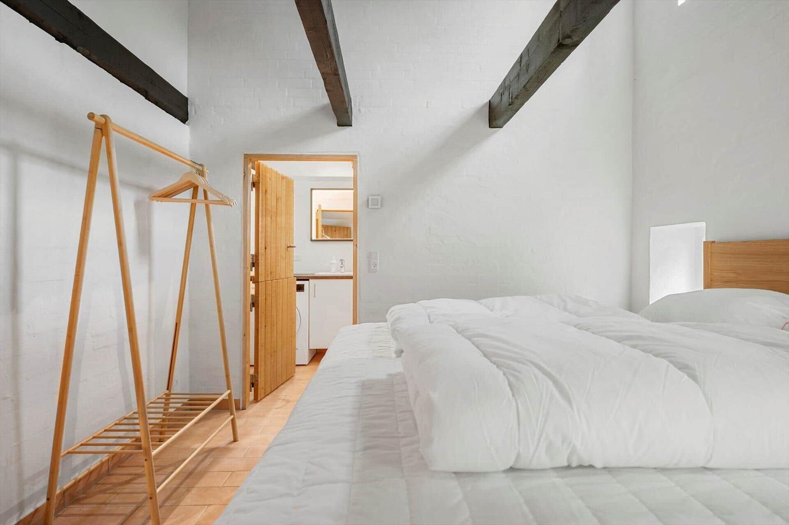 Bedroom with white bed, wooden stand, and view into bathroom.