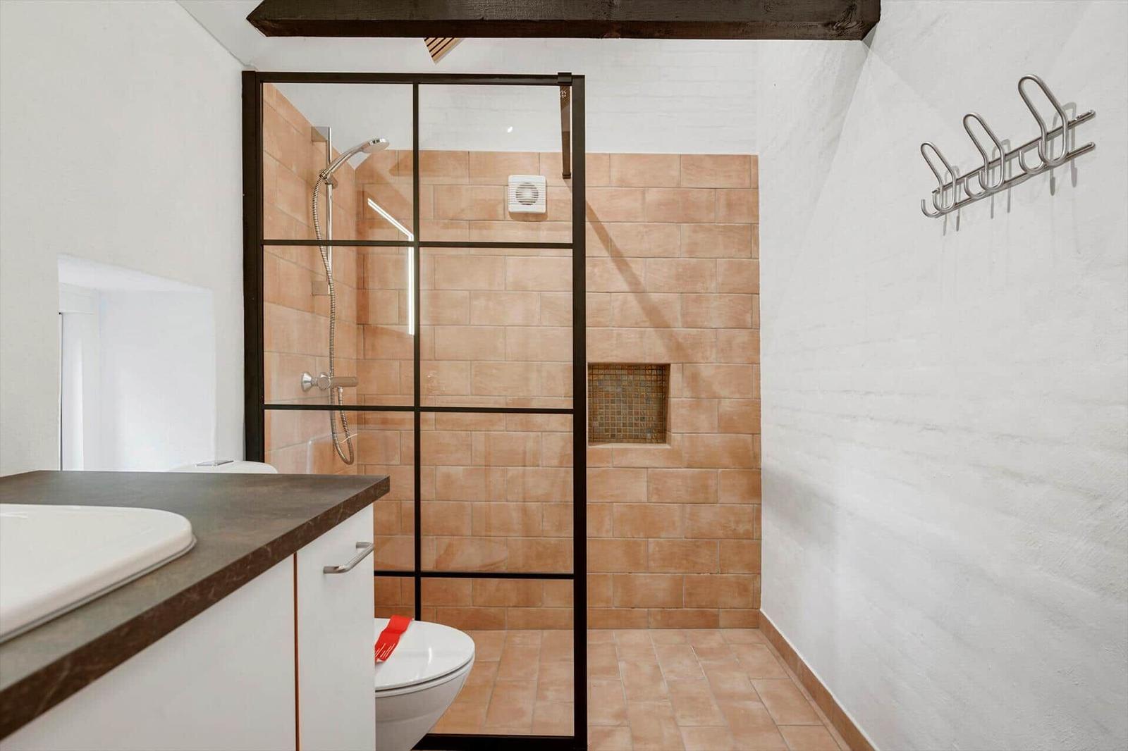 Bathroom with shower, sink, and toilet. Walls covered with terracotta tiles.